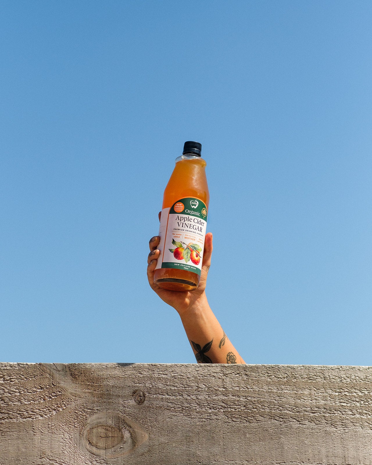 Hand holding a bottle of CoralTree apple cider vinegar against a clear blue sky