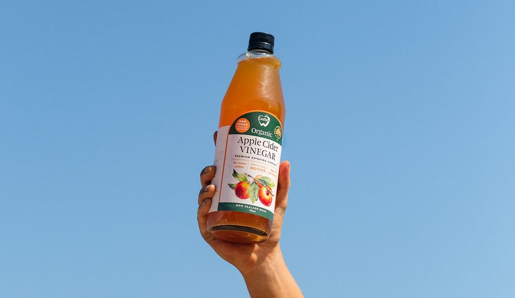 CoralTree Apple Cider Vinegar being held in the air with the clear blue sky in the background.