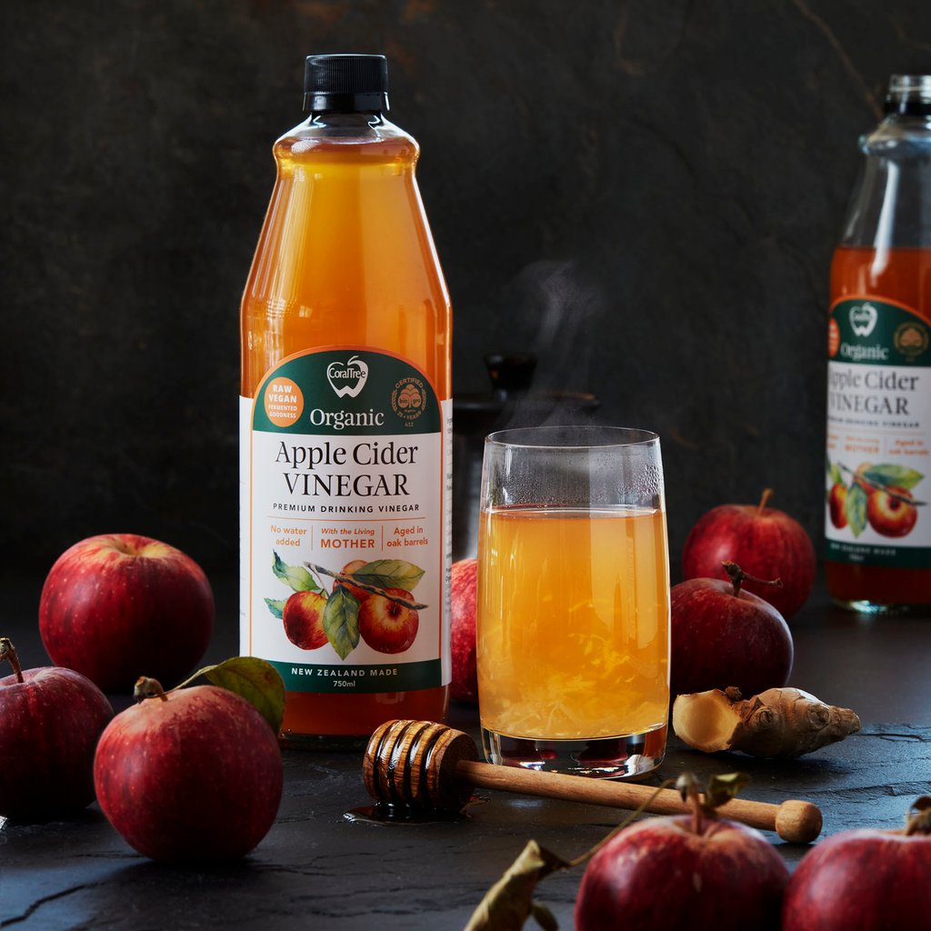 CoralTree Bottle next to a glass of Apple Cider Vinegar mixed with water and honey and ginger. Apples sit next to the bottle.