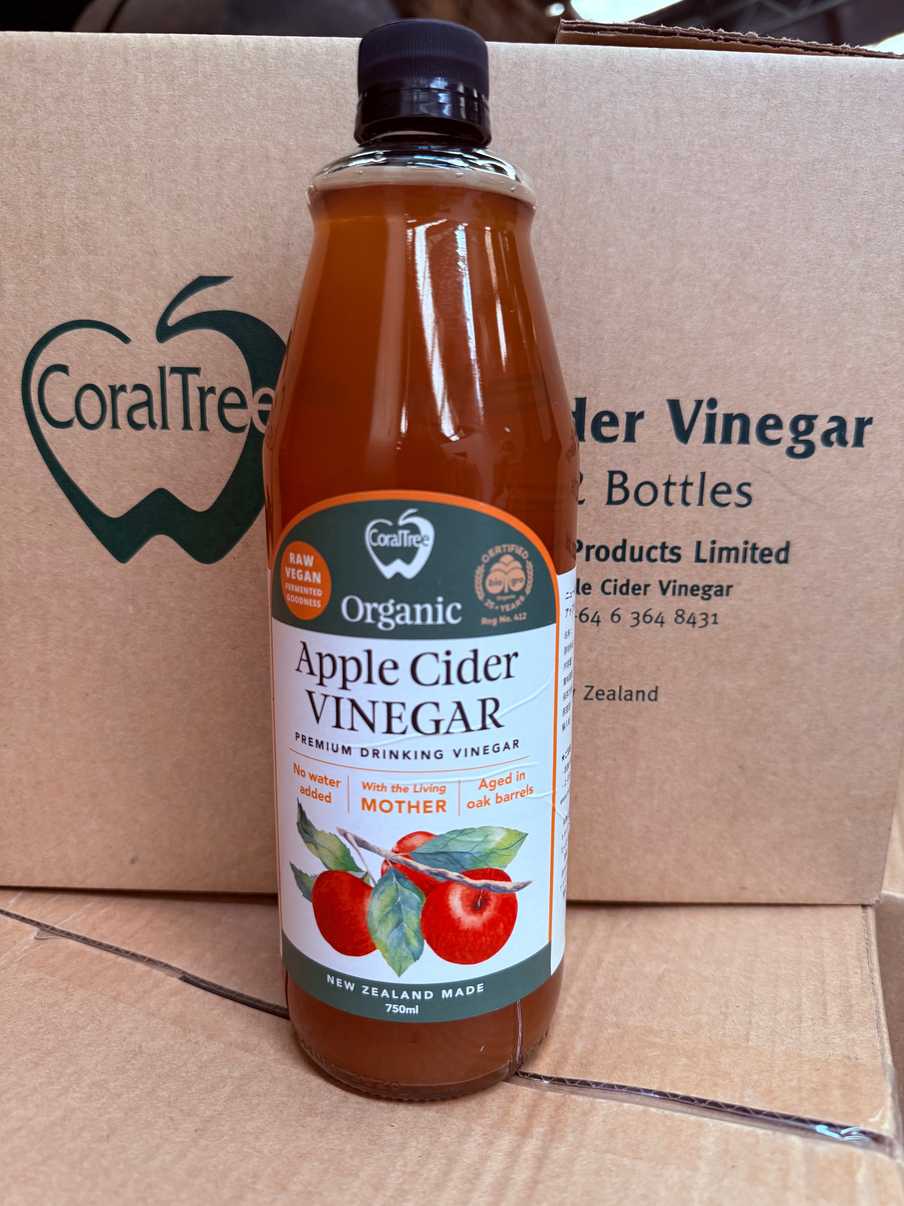 A bottle of CoralTree Organic Apple Cider Vinegar placed in front of a branded cardboard shipping box.