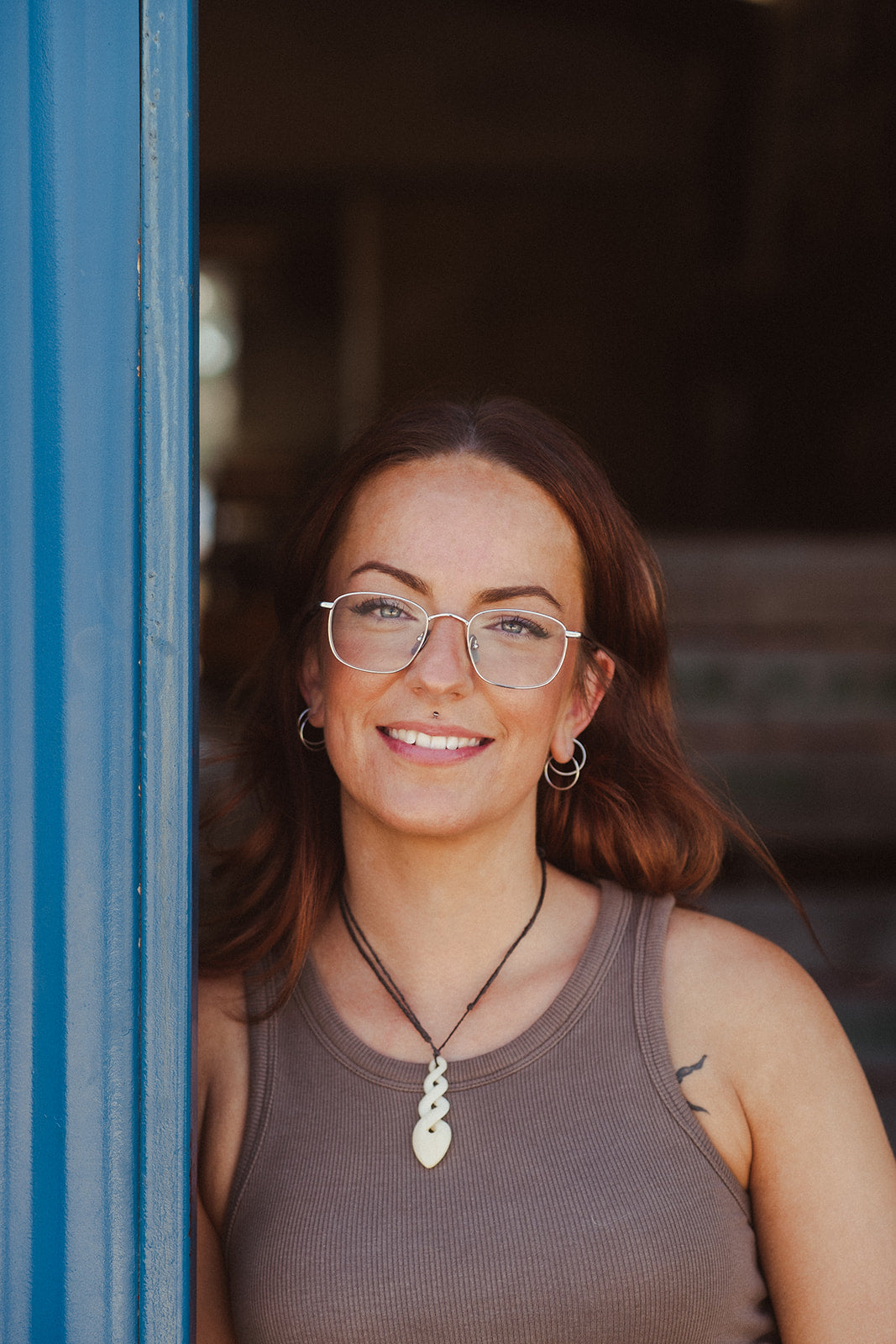 Zhana Baker wearing glasses and a brown tank top, standing in a doorway.