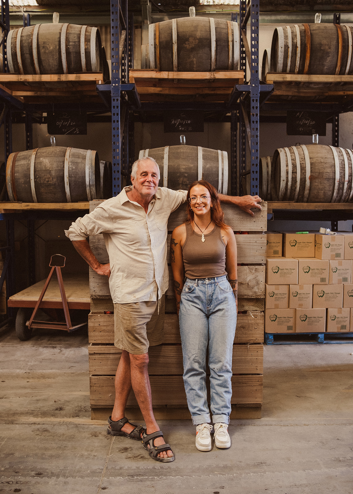 Photo of Kim Baker and Zhana Baker in CoralTree Organics warehouse. Oak barrels full of Apple Cider Vinegar behind them. 