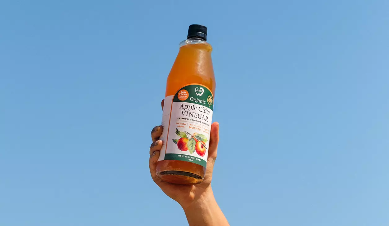 A hand holds CoralTree's 750ml bottle of Apple Cider Vinegar in the sky.